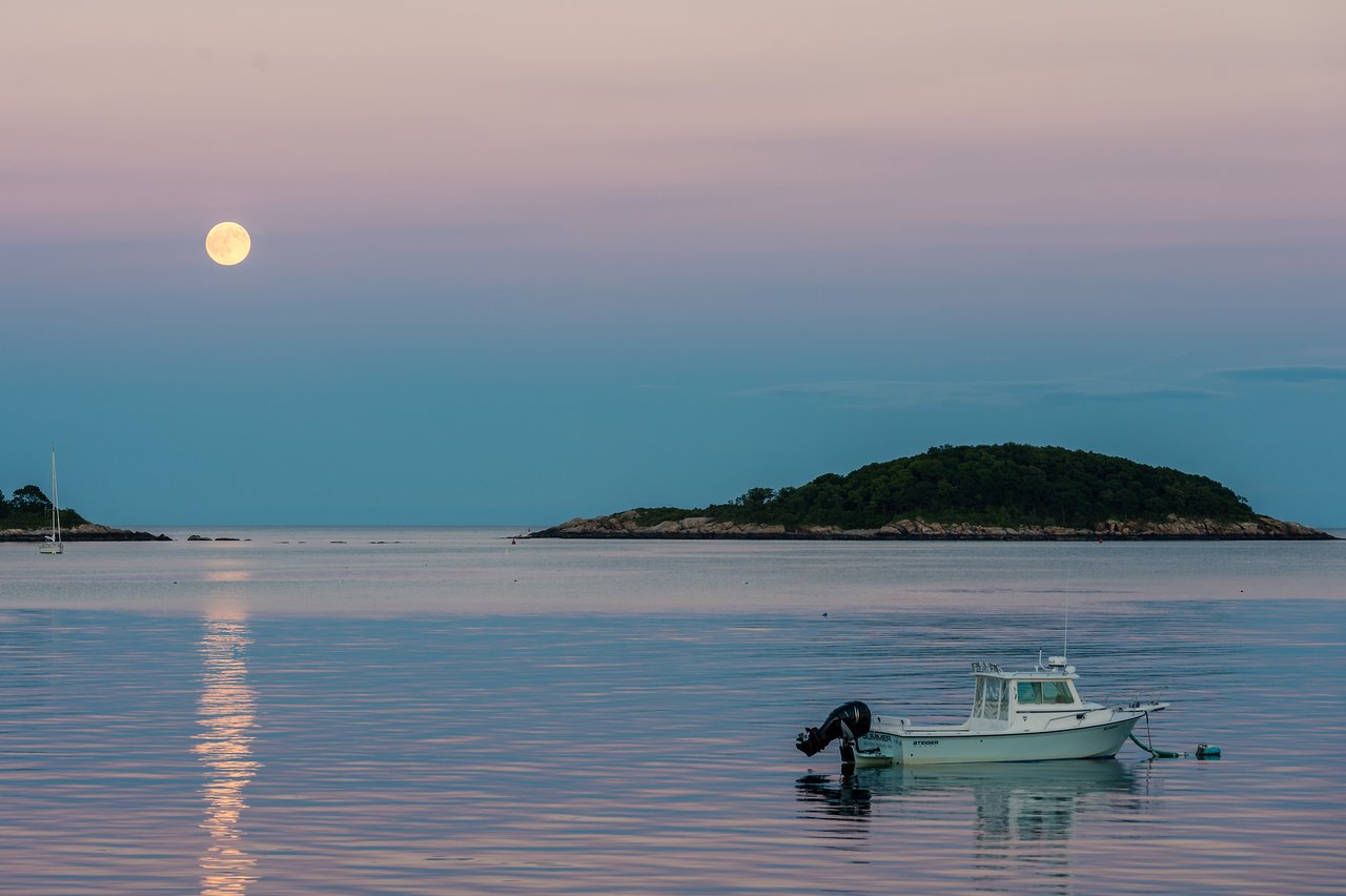 Full moon reflecting on calm ocean water with a small boat floating near an island.
