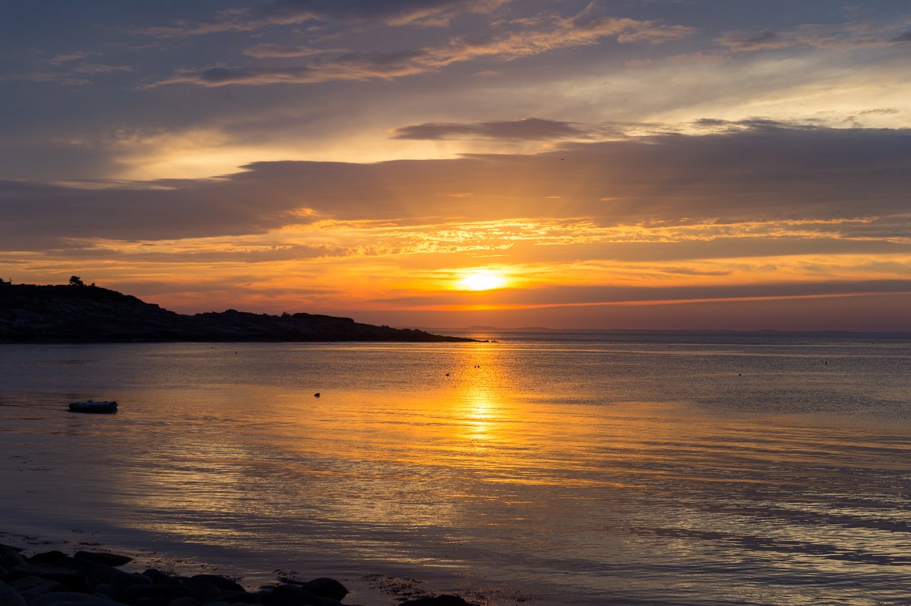 The sun sets over calm coastal waters, casting a golden reflection.