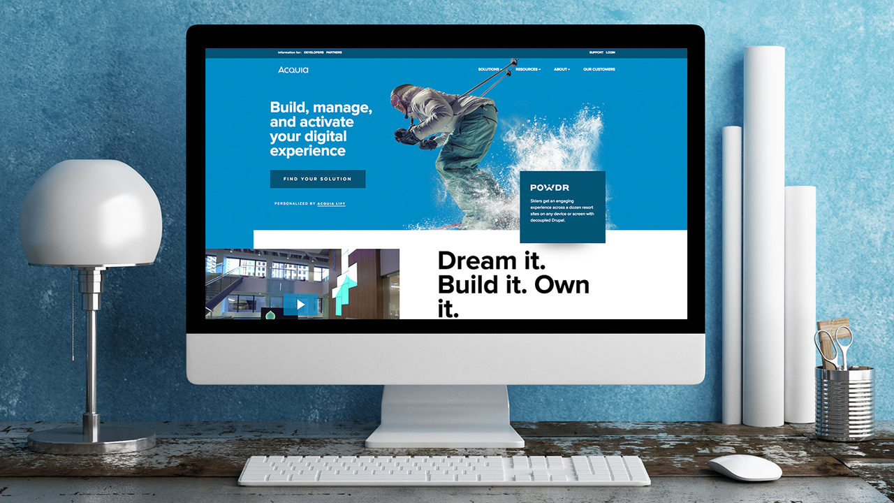 A computer screen shows the Acquia website with a slogan about building and managing digital experiences.