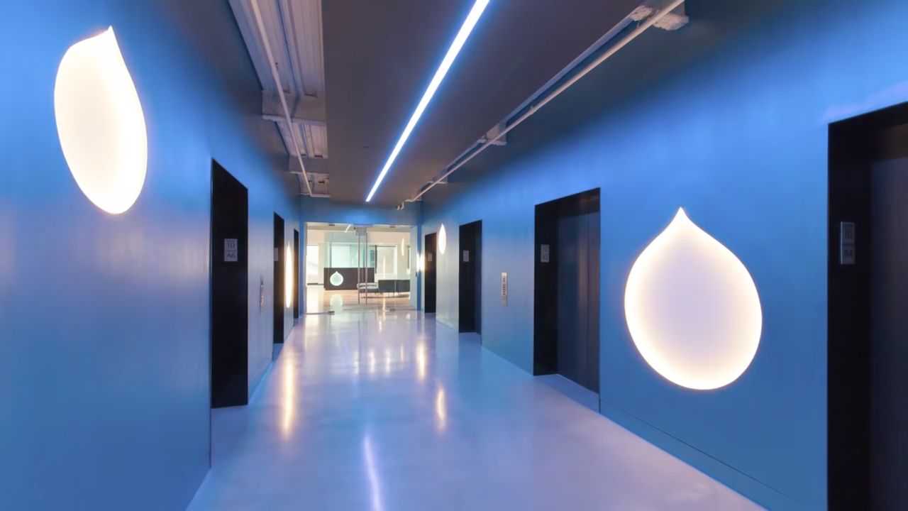 A modern office entrance with blue walls, illuminated droplet logos, and elevators on both sides.