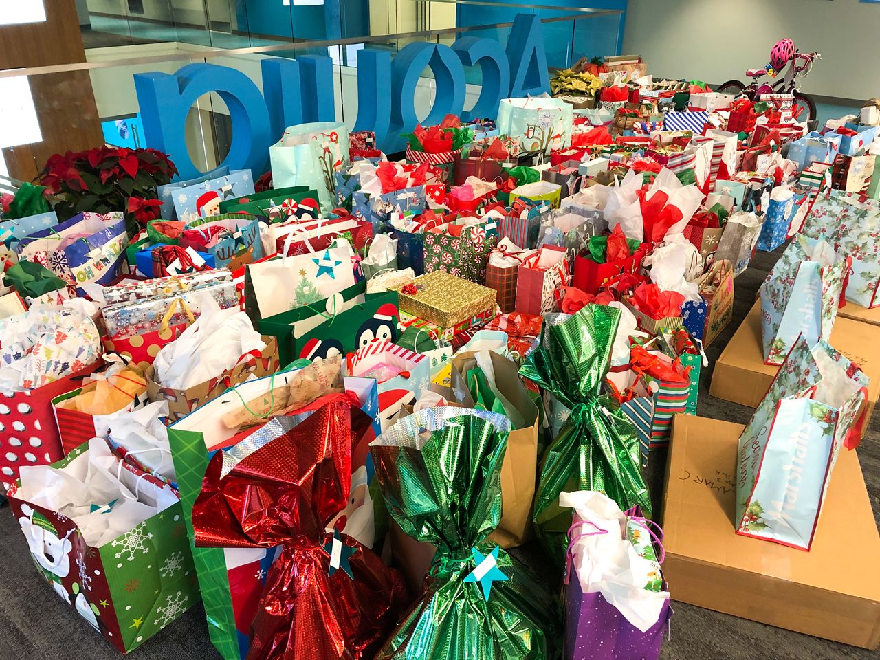 A large collection of colorful gift bags and boxes arranged for a holiday gift drive in an office space.