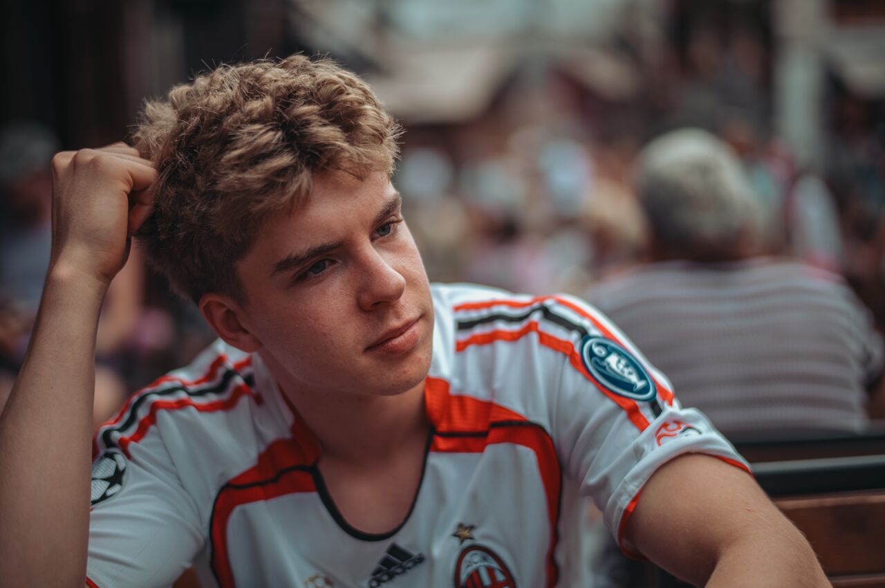 A young man in a soccer jersey rests his head on his hand and looks to the side.
