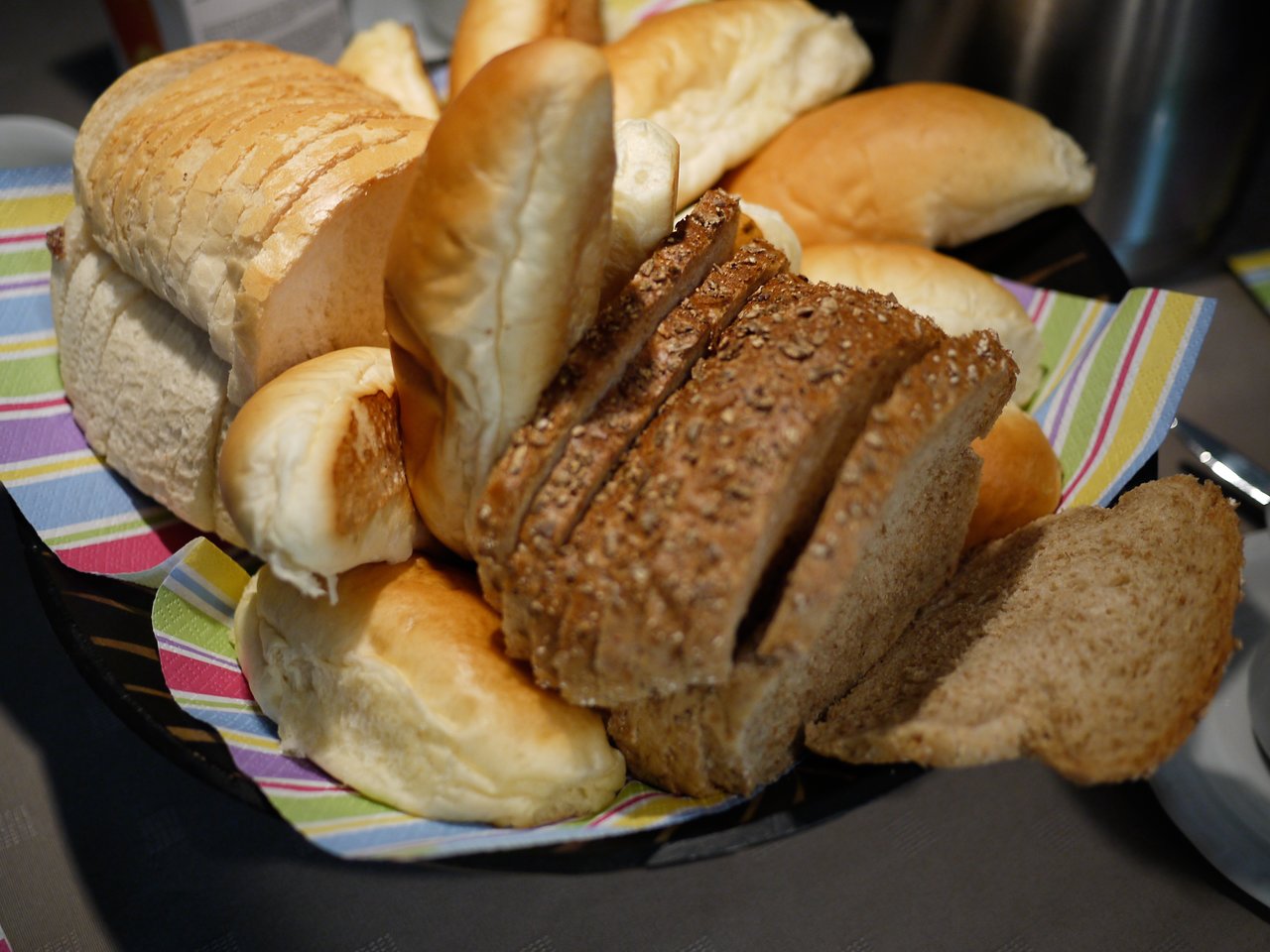 A basket filled with various types of bread, including sliced whole grain and soft white rolls, on a table.