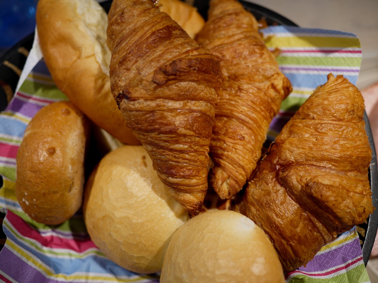 A basket filled with croissants and bread rolls on a colorful napkin, ready to be served for lunch.