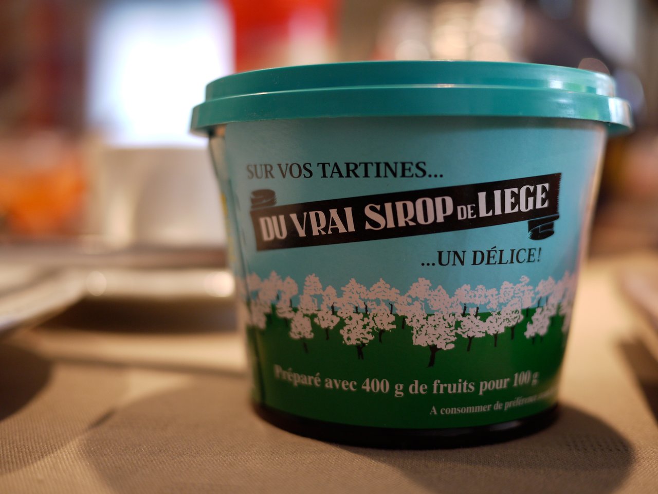 A container of "Sirop de Liège" fruit spread sits on a table, likely part of a meal.