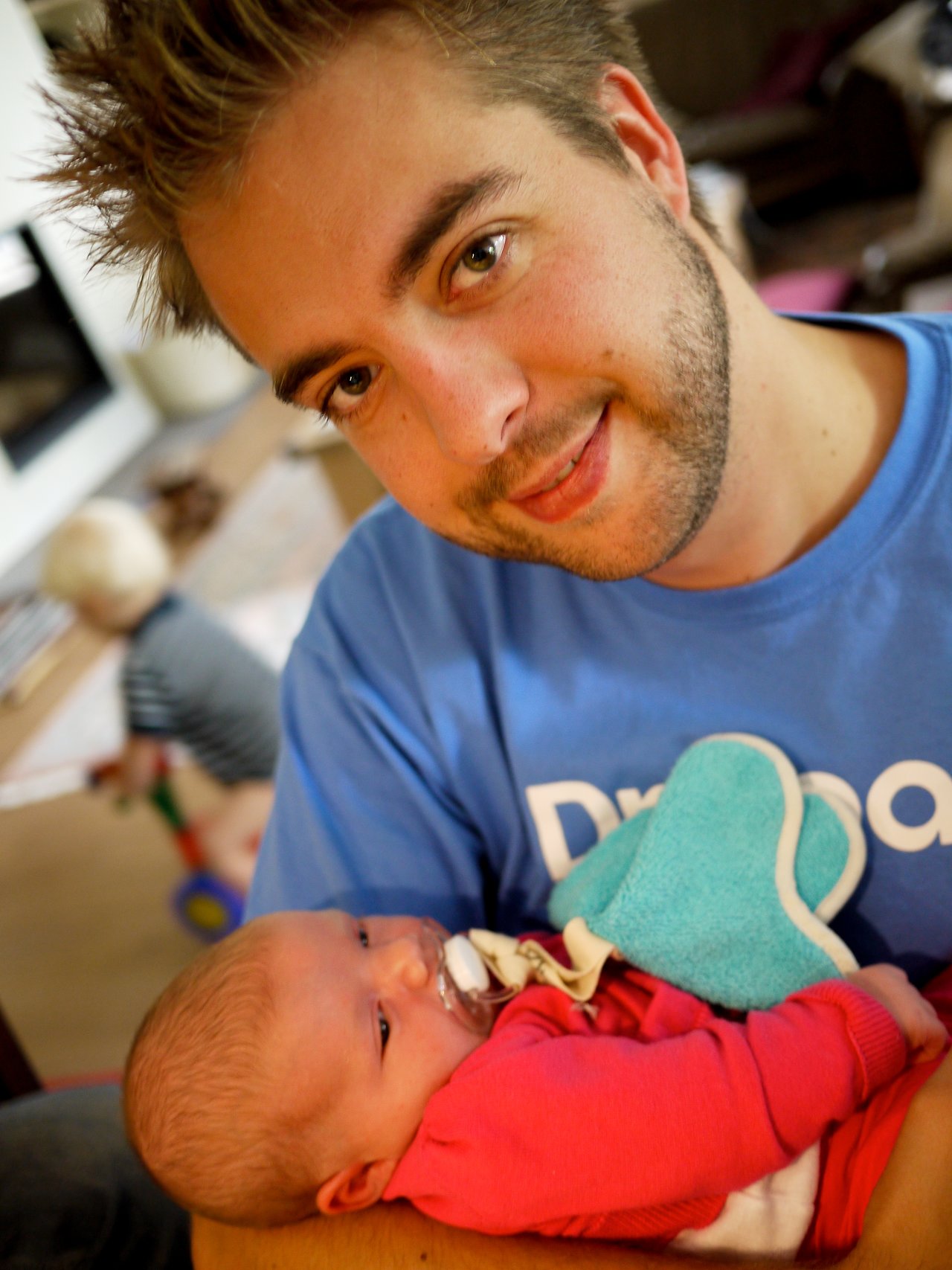 A man in a blue shirt holds a newborn baby with a pacifier and a small blanket.