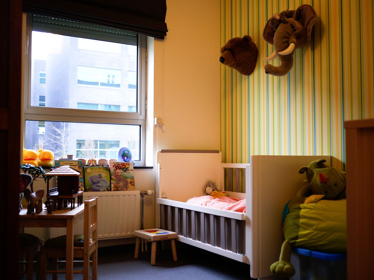 A children's bedroom with a crib, stuffed animals, books, and a small table with chairs near the window.