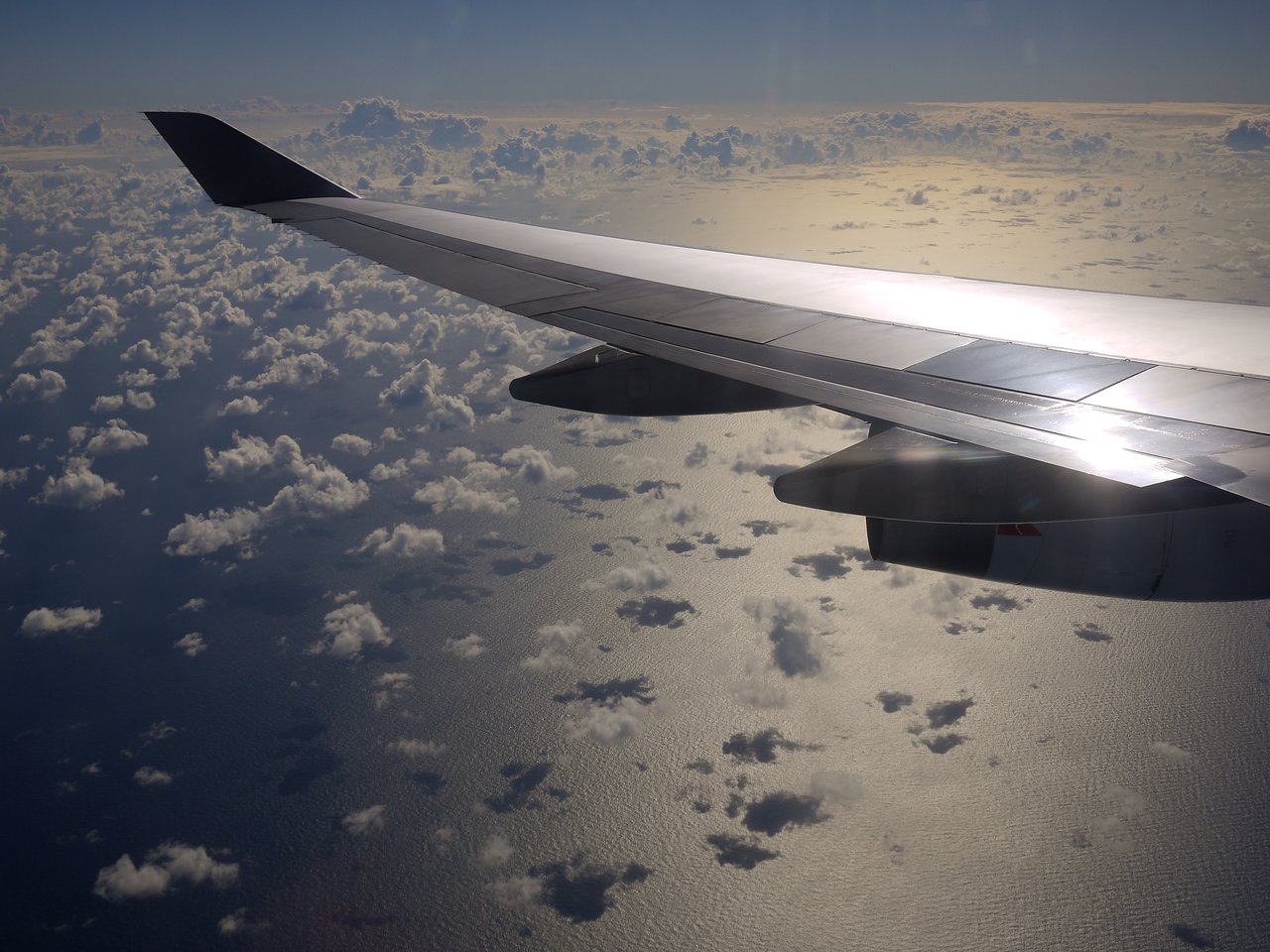 View from an airplane window showing the wing and clouds below while approaching Brisbane for landing.