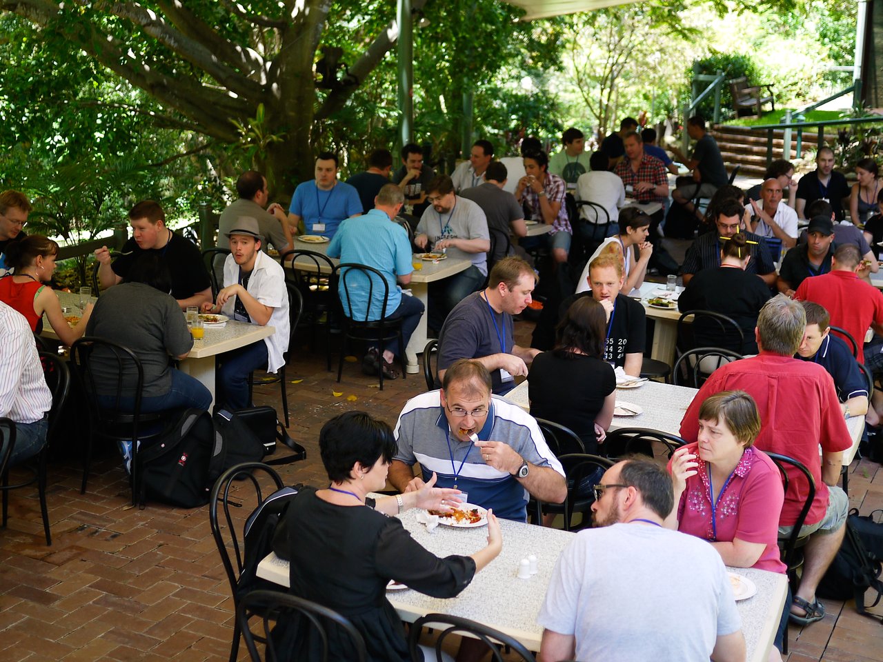 People wearing conference badges are gathered at outdoor tables, eating and talking during the Drupal Downunder conference in 2011.