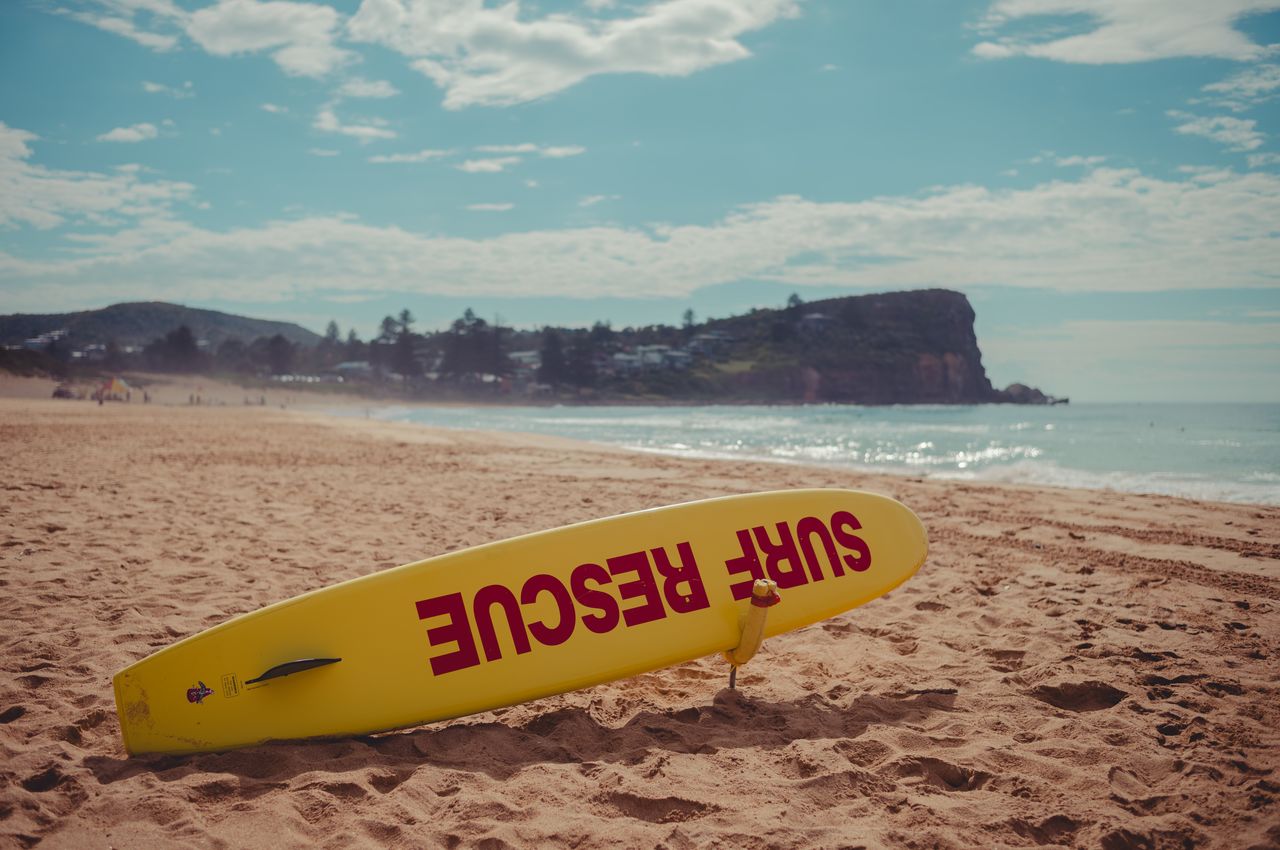 A yellow surf rescue board on a beach with the words 'Surf rescue'.