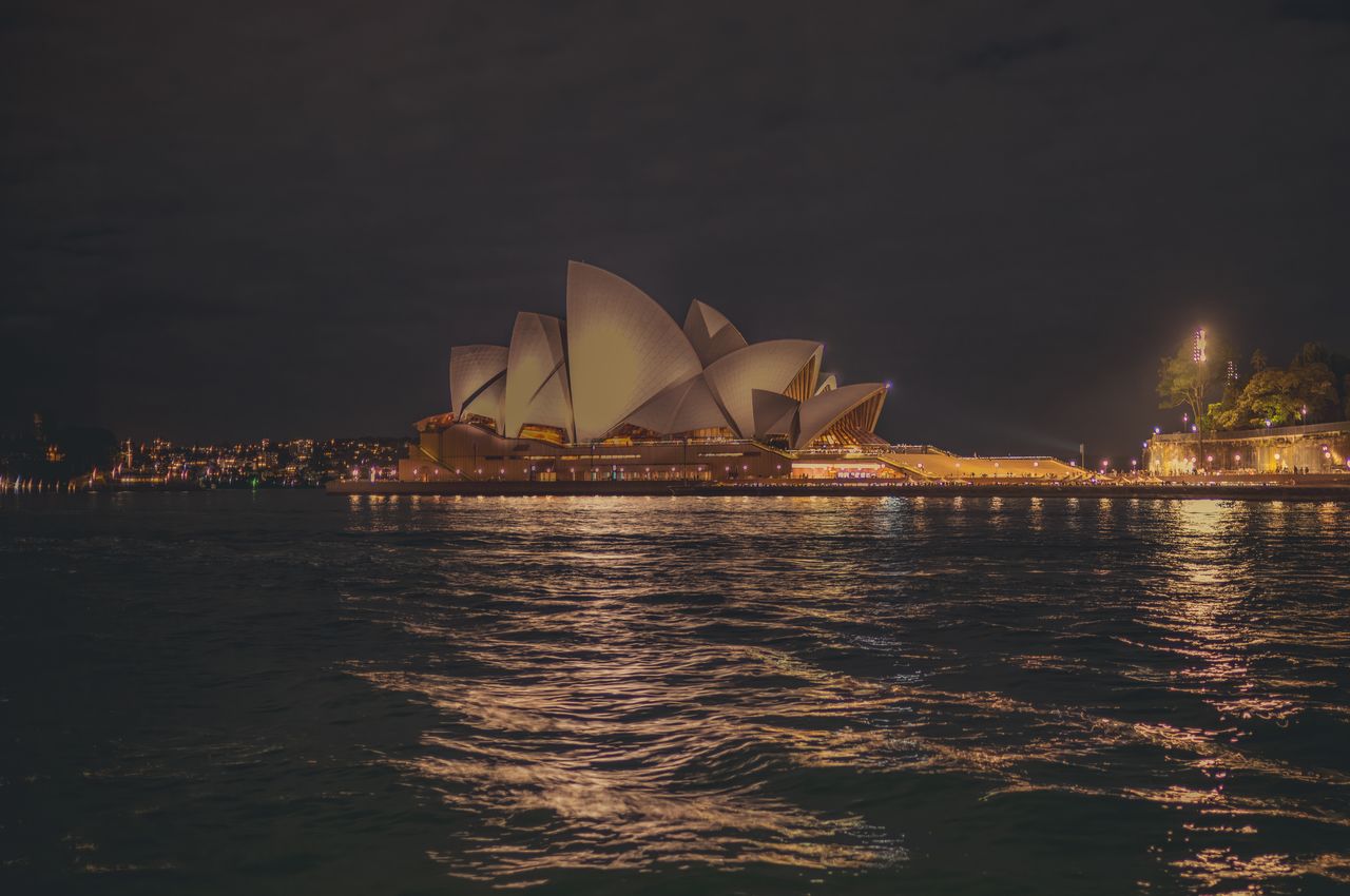 The Sydney Opera House at night, with lights reflected in the water.