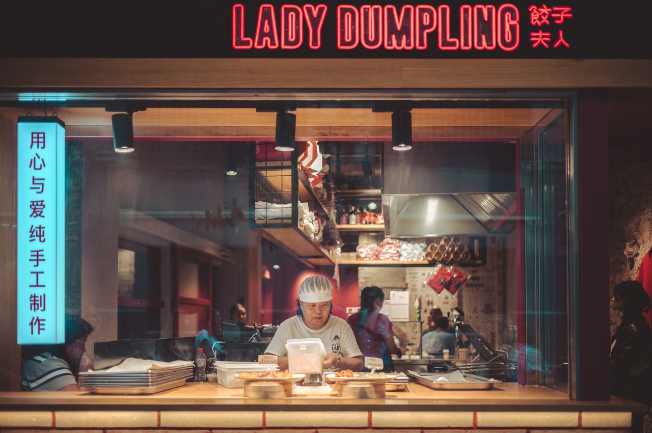 A chef making dumplings viewed through a restaurant window.