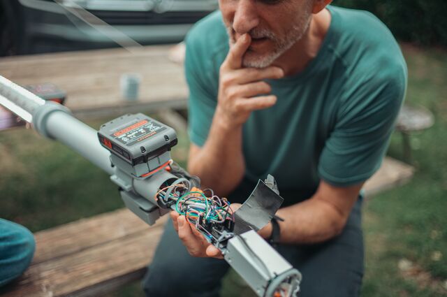 A man rests his hand on his chin while examining a tangle of colorful wires.