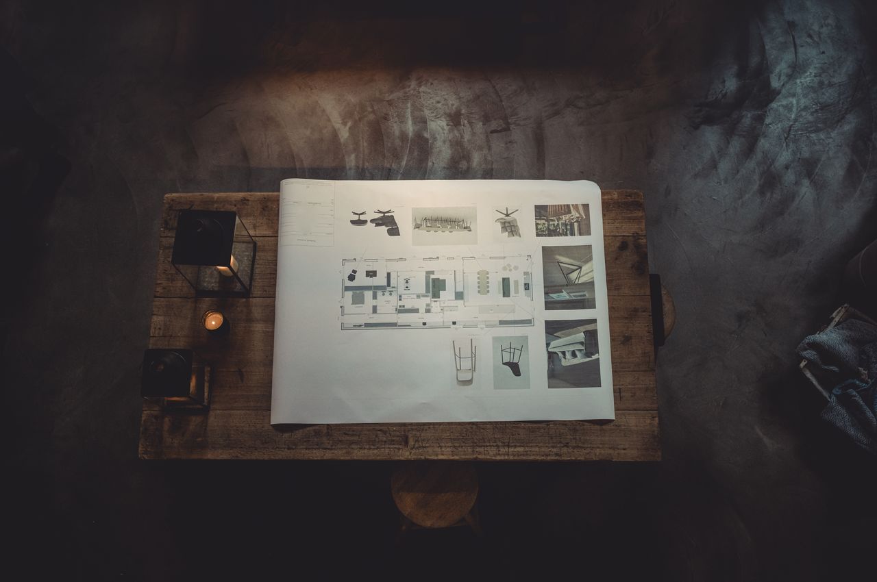 An aerial shot of an old wooden table with a large printout of a floor plan. The floor plan provides has illustrations of chairs and sofas printed on it.