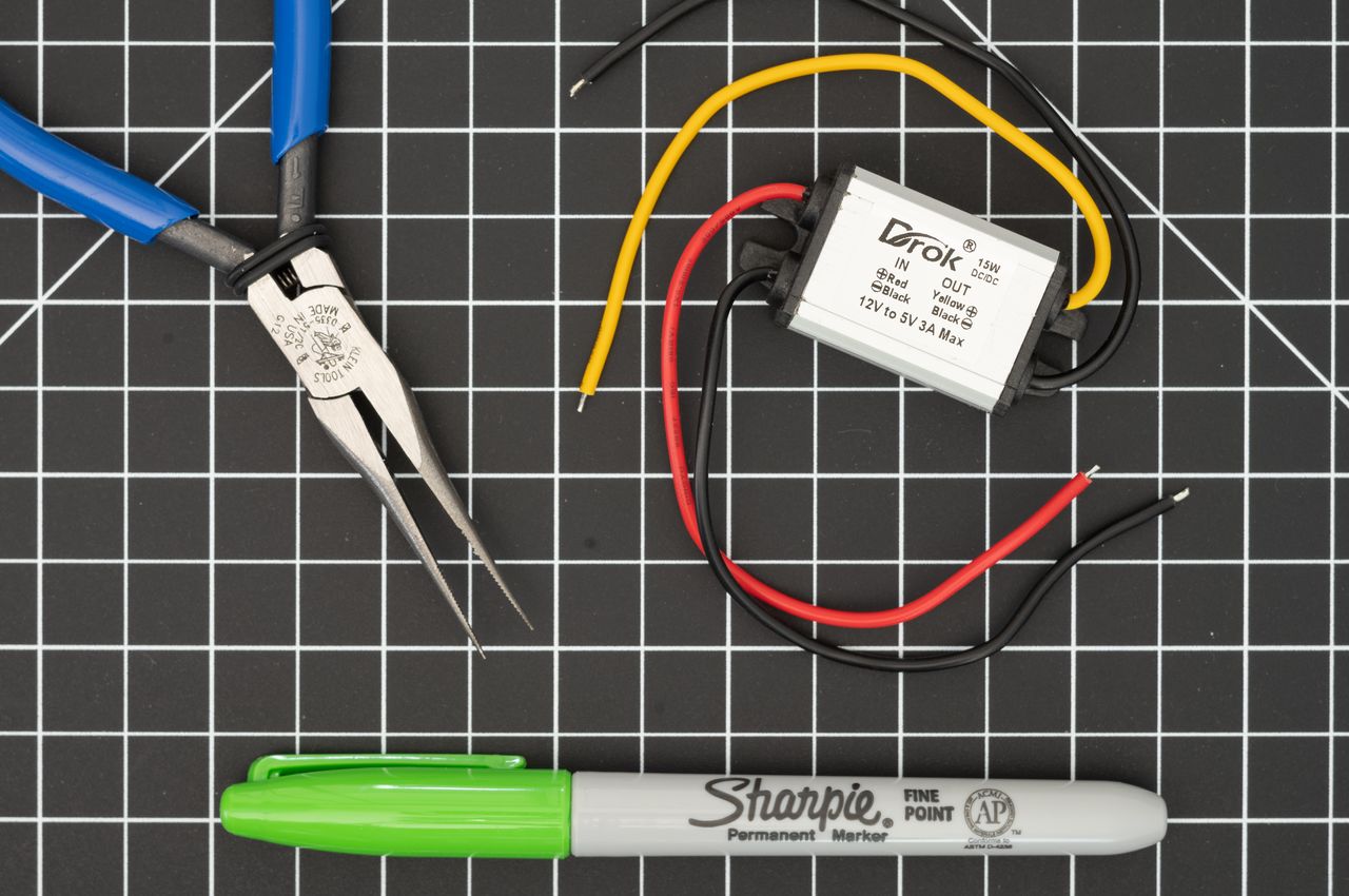 A 12V to 5V voltage converter in a waterproof metal box the size of a matchbox, placed on a gridded mat.