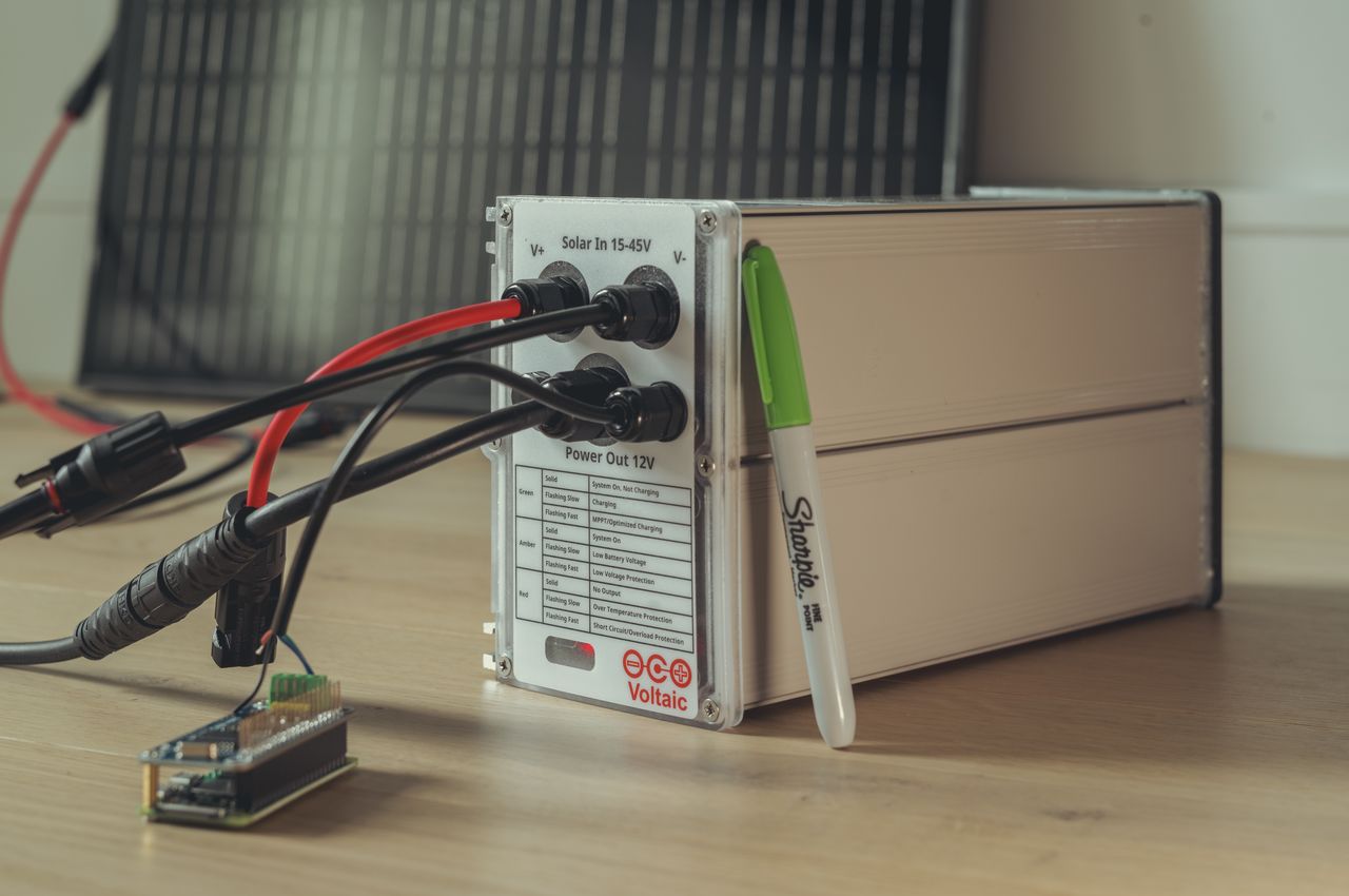 A large battery, the size of a loaf of bread, with a solar panel in the background.