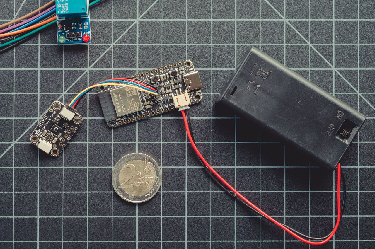 An ESP32-S3 development board is linked to an SHT41 temperature and humidity sensor and powered by a battery pack. For scale, a 2 Euro coin is included. The SHT41 sensor is roughly equivalent in size to the coin, and the ESP32-S3 board is about twice the coin's diameter.