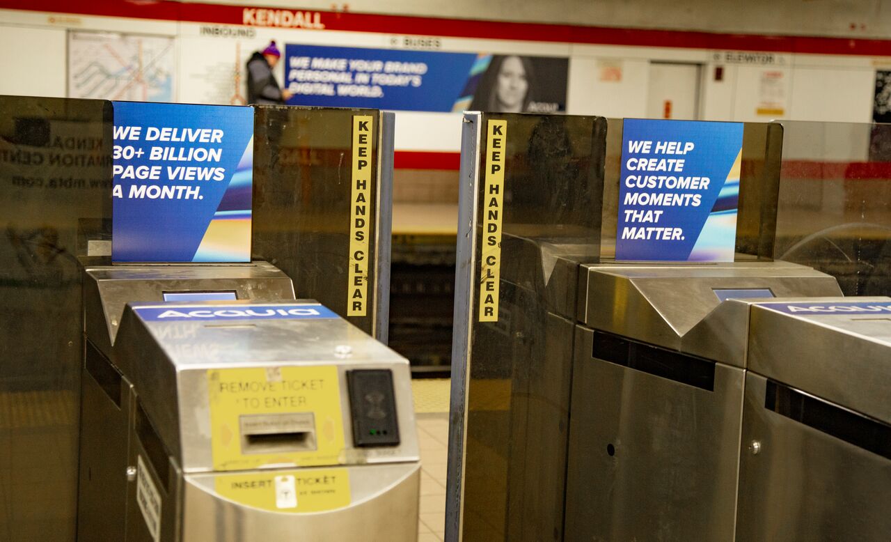 Turnstiles at Kendall Square station display Acquia advertisements with messages about page views and customer engagement.