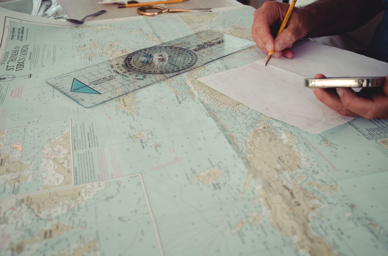 A hand on top of a nautical chart and next to a course plotter