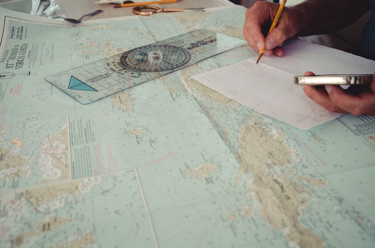 Navigation planning A hand on top of a nautical chart and next to a course plotter