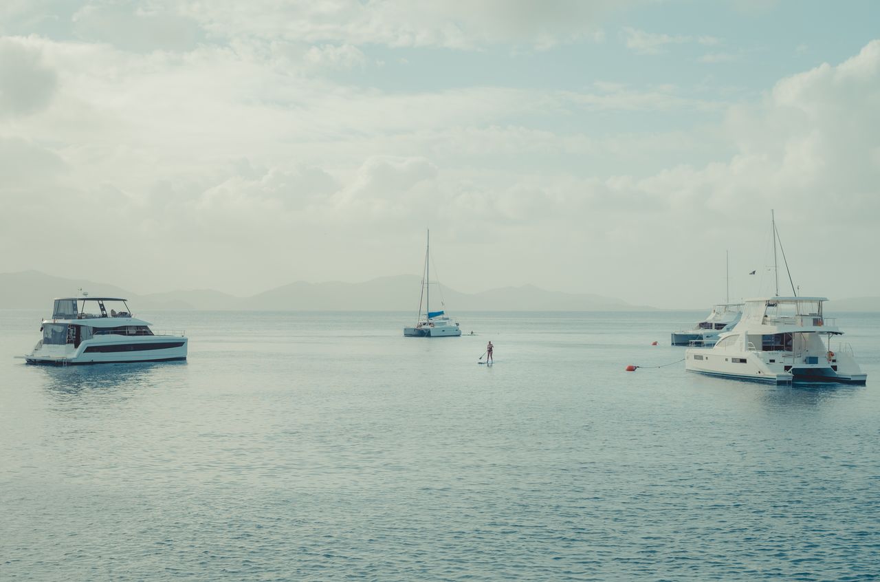 A woman standing on a paddle board, surrounded by boats on mooring balls