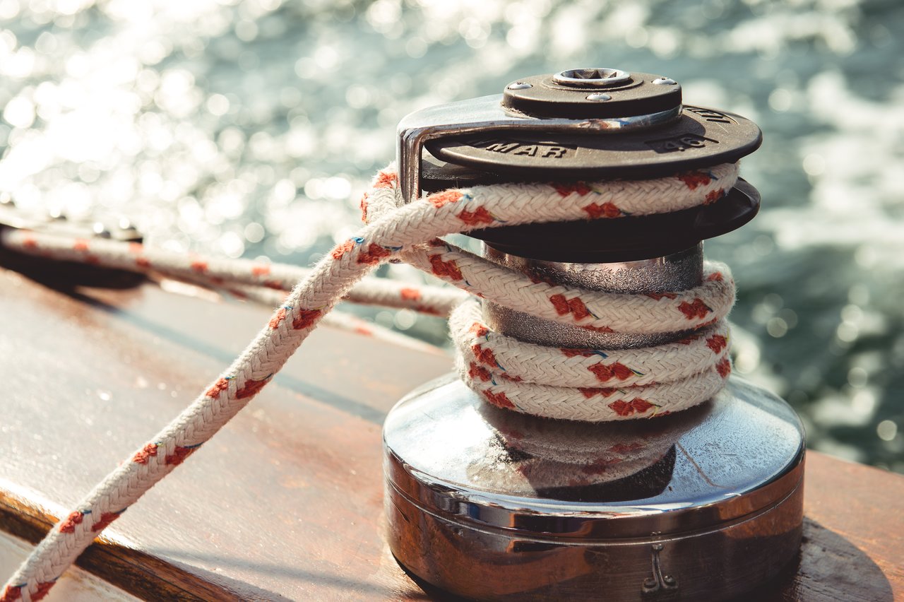 A close-up of a sailing winch with a rope wrapped around it, secured on a boat with water in view.