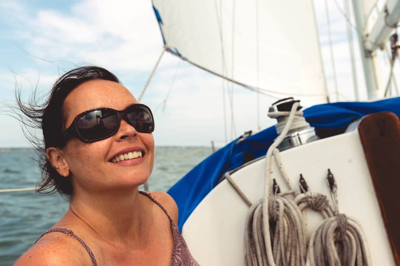 A woman wearing sunglasses smiles while sailing on a boat.