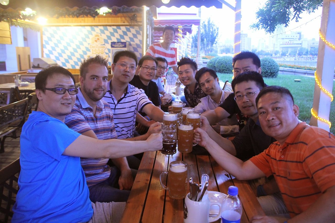 A group of people at an outdoor table raising beer glasses and smiling during a Drupal meetup in Tianjin.