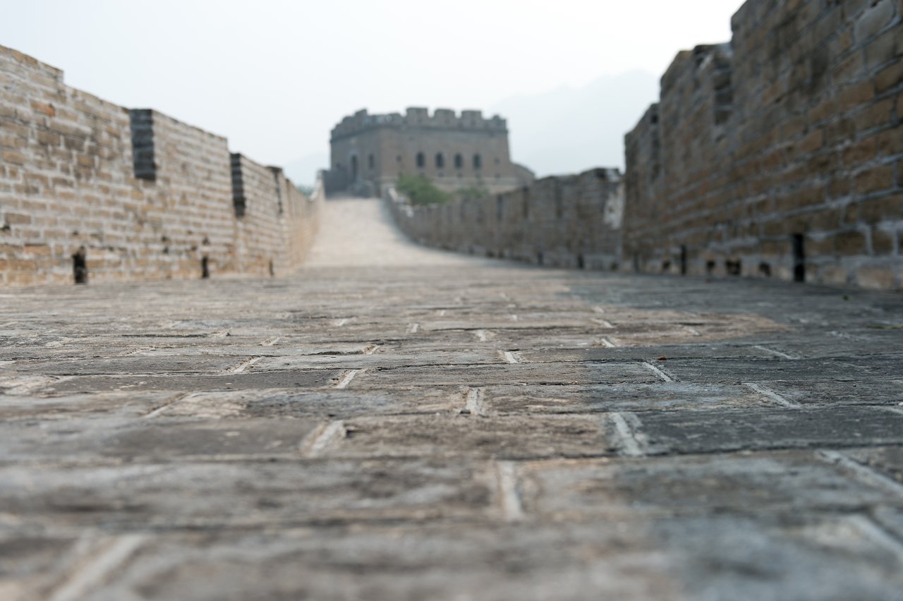 A low-angle view of the Great Wall of China, showing a stone pathway leading to a watchtower in the distance.