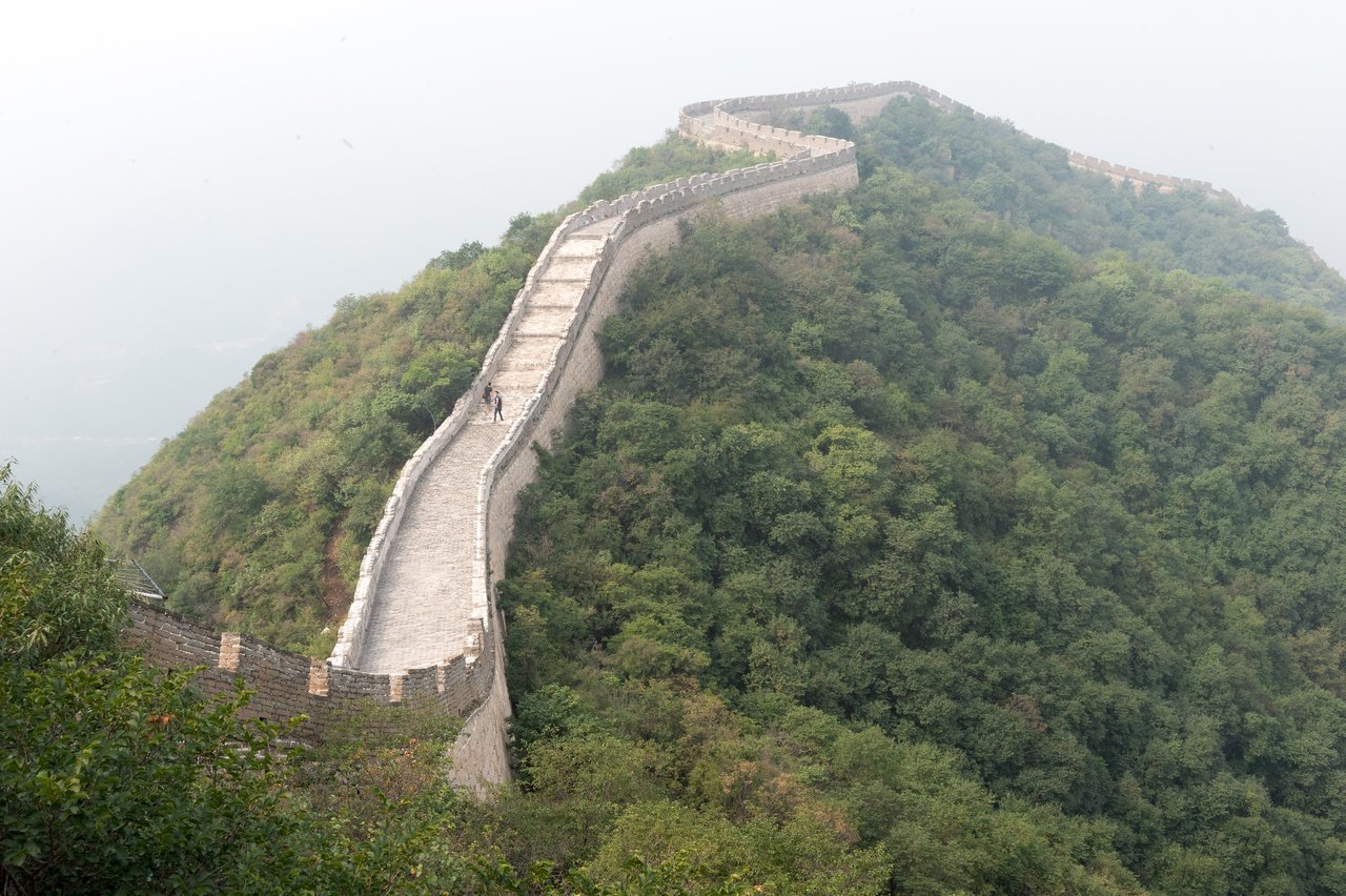 A section of the Great Wall of China stretches over a green hillside, with a few people walking.