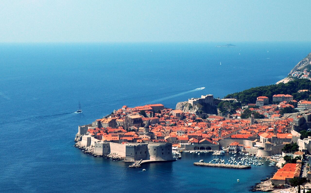 Aerial view of Dubrovnik's old town with stone walls, red rooftops, and boats in the surrounding sea.