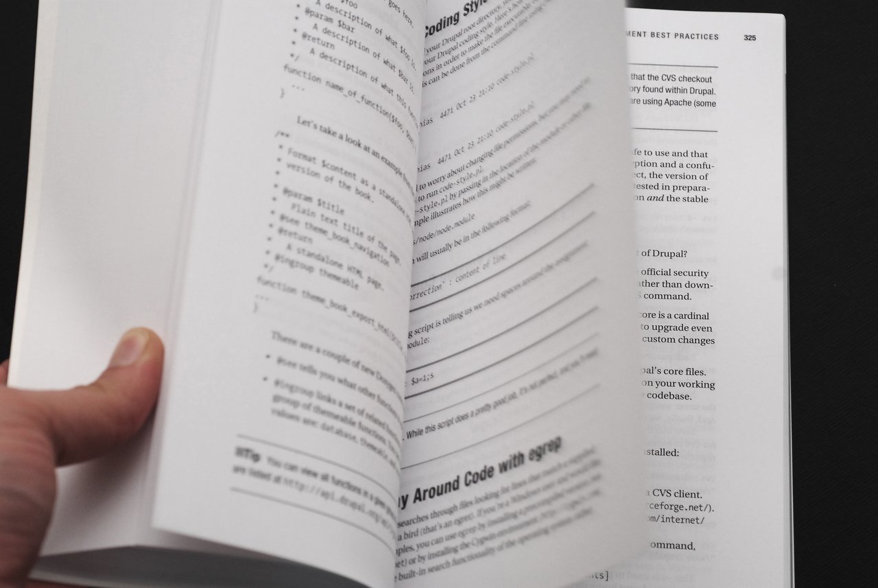 A person flips through the pages of a technical book about Drupal development, showing code and text.