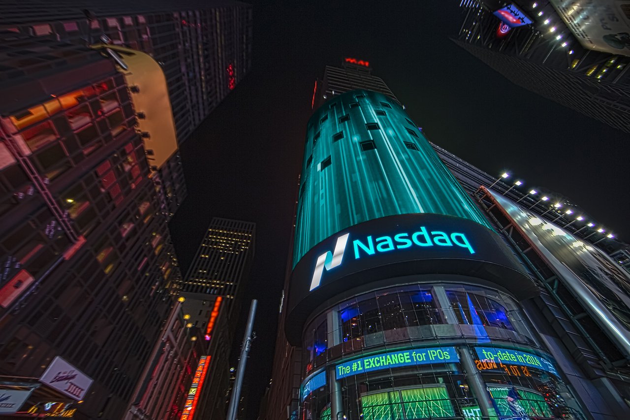 A Nasdaq building at night with bright digital signs displaying stock market information.