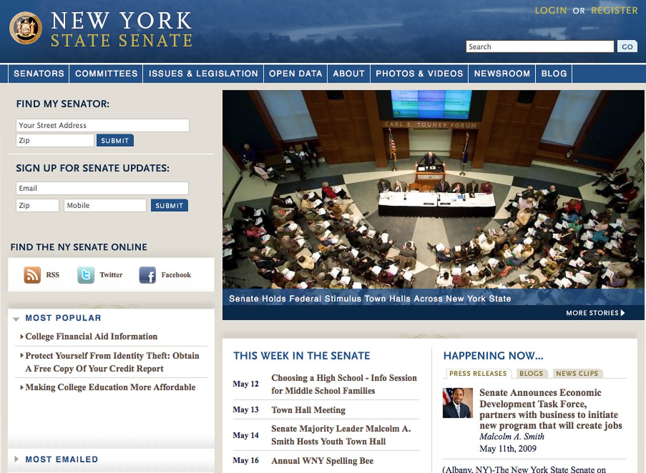 A town hall meeting in a large auditorium with a speaker at a podium addressing an audience and panelists.