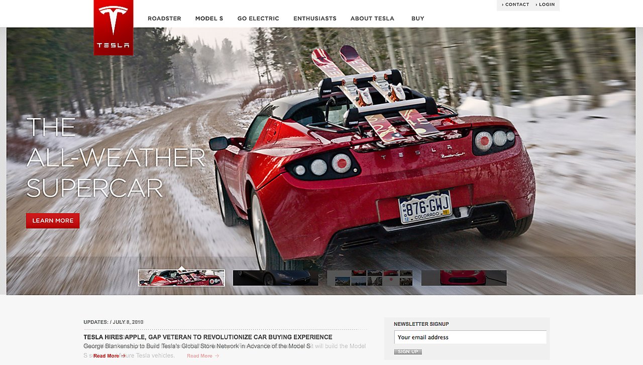 A red Tesla Roadster drives on a snowy road with skis mounted on the back.