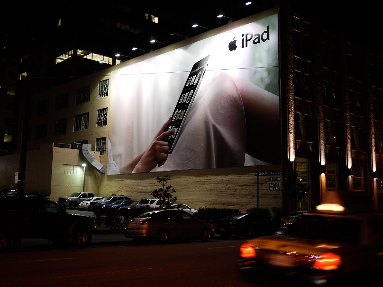 Large billboard advertisement for the Apple iPad at night, showing a hand interacting with the tablet's screen.