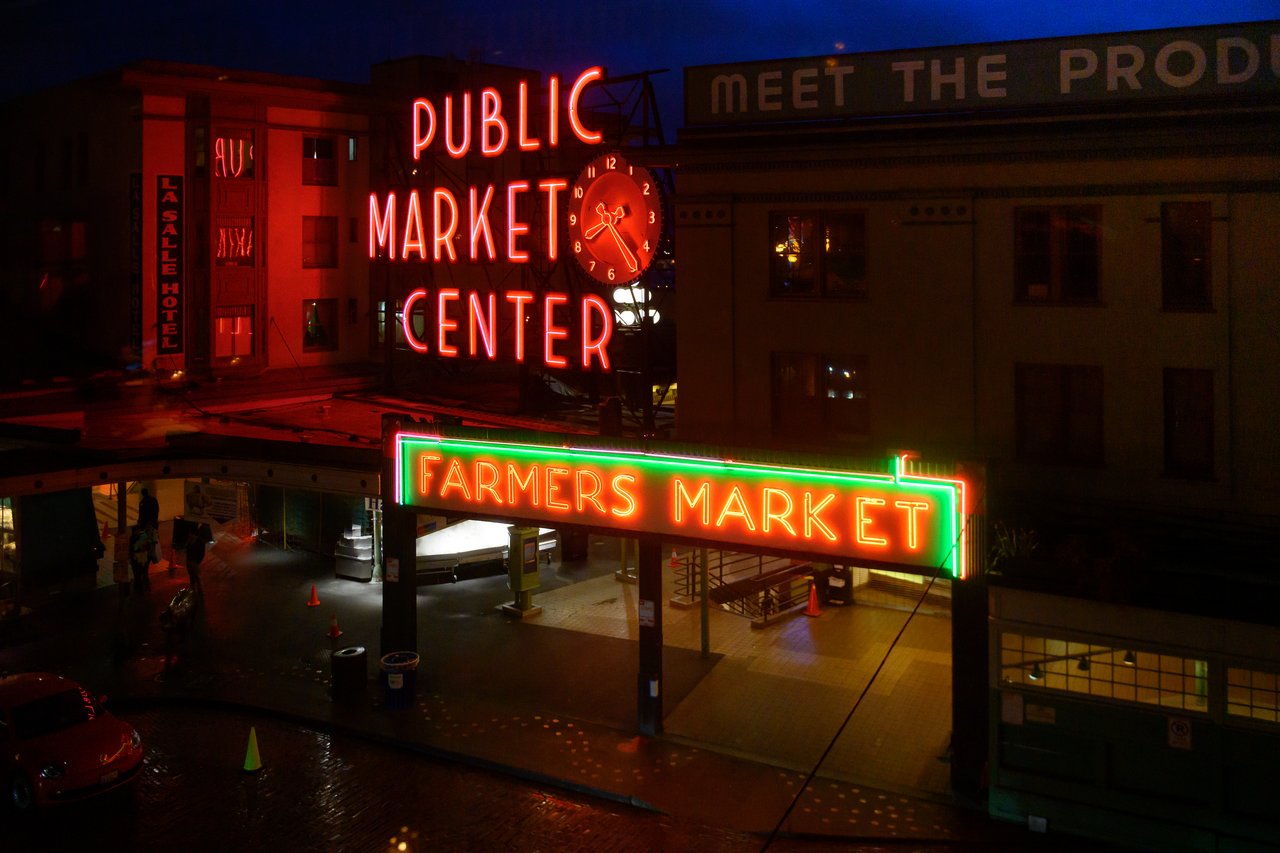 Neon signs for "Public Market Center" and "Farmers Market" glow at night in Seattle's famous Pike Place Market.