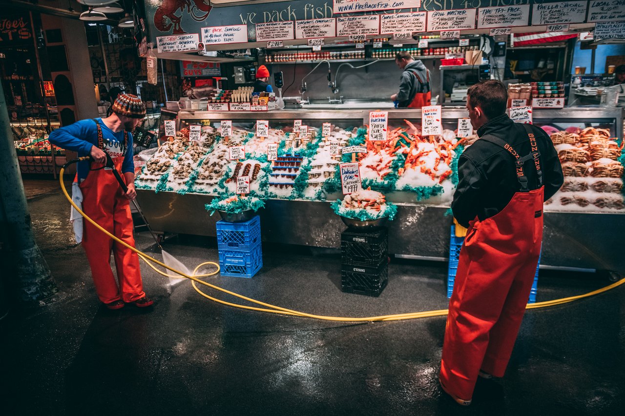 Workers in red aprons clean the floor near a seafood stand at a public market in Seattle.