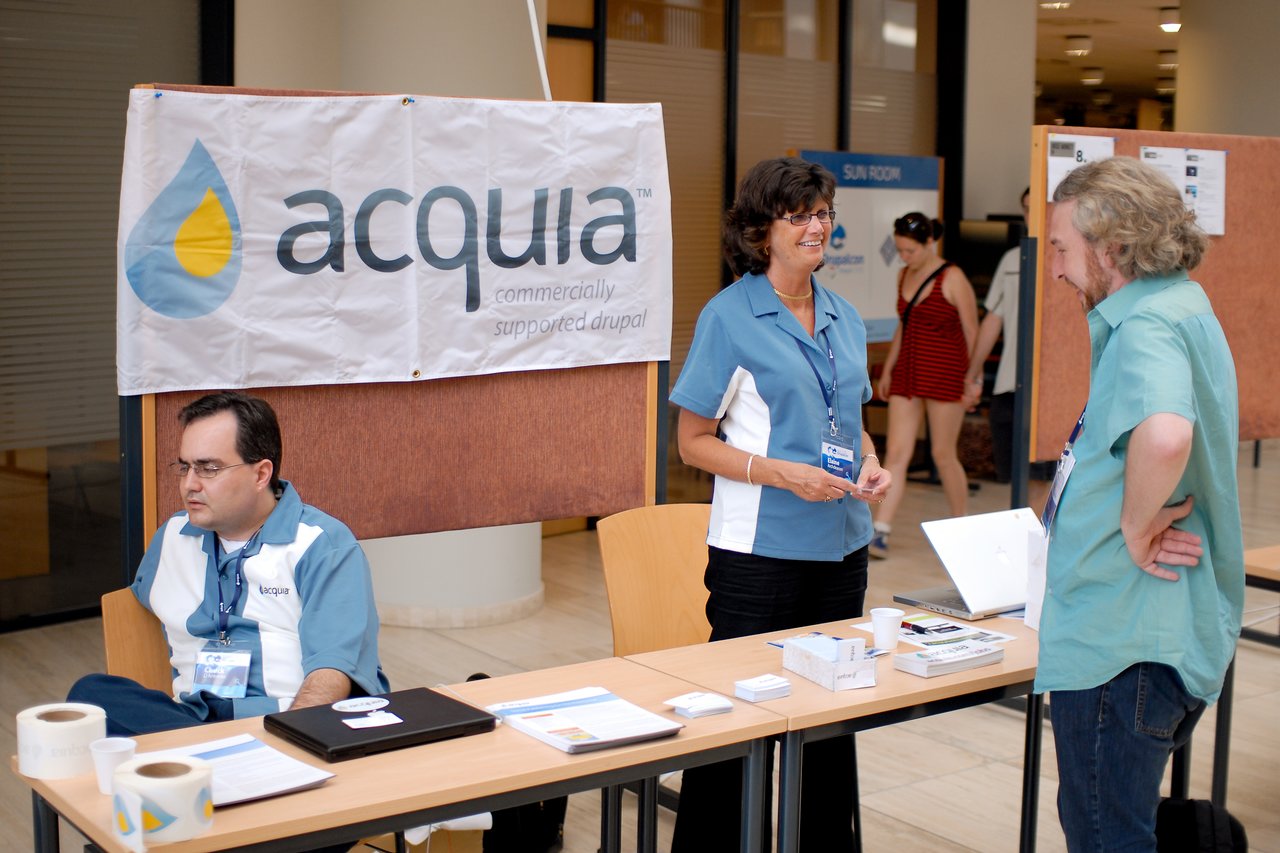 A woman at the Acquia booth talks to a visitor while another staff member sits at the table.