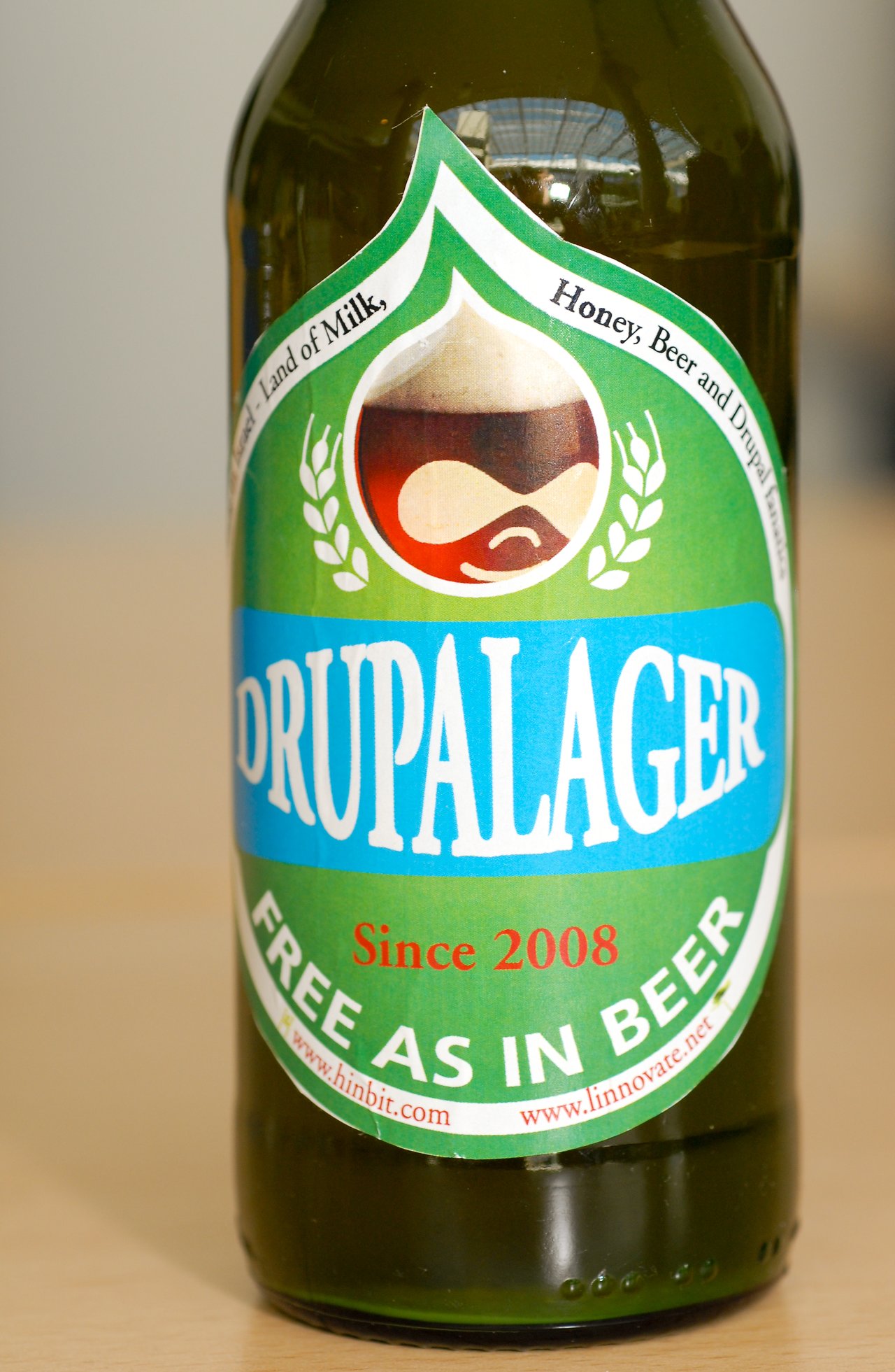 A close-up of a beer bottle labeled "Drupalager" with a Drupal-themed design and the phrase "Free as in Beer.