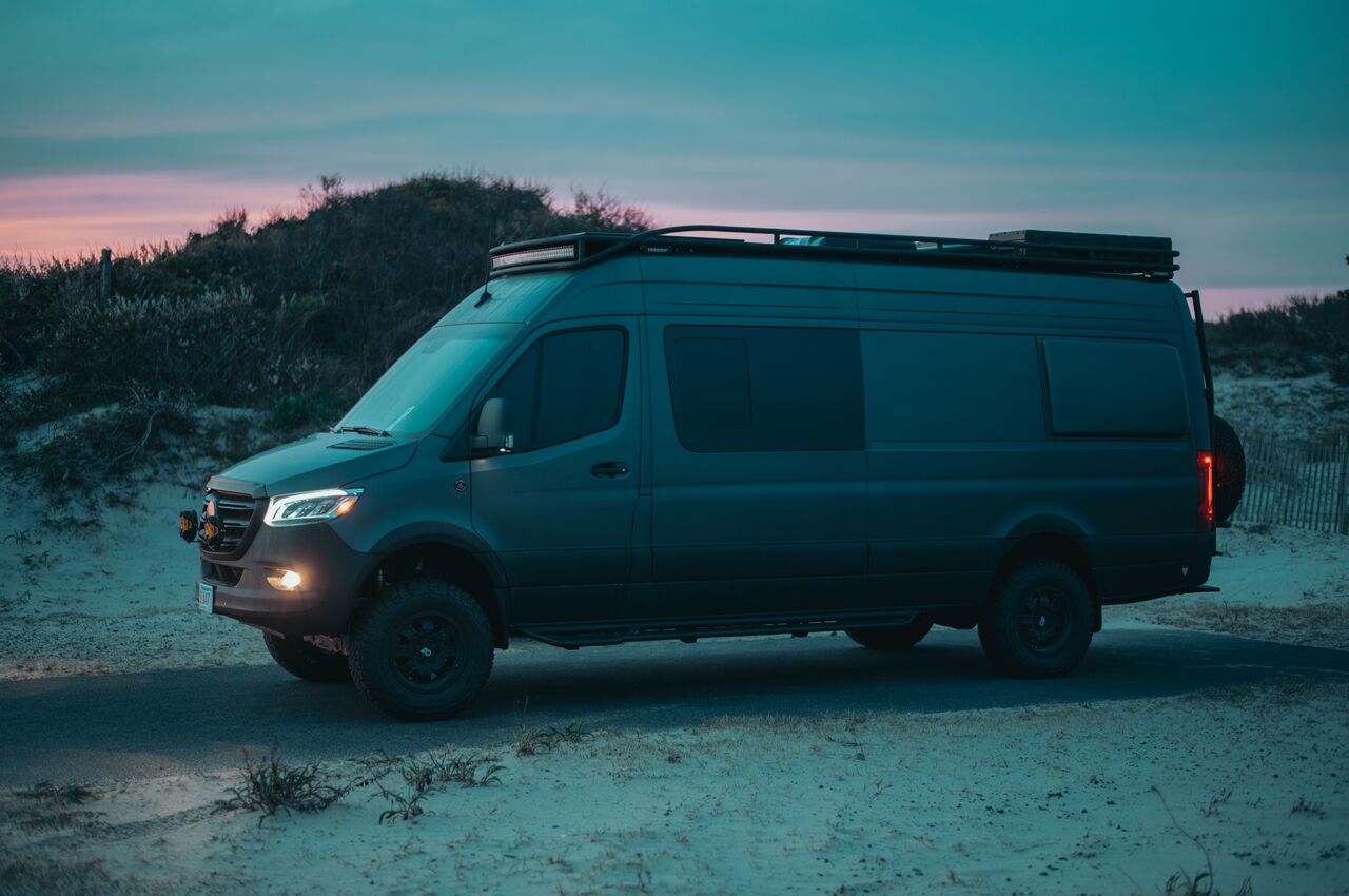 Matte black camper van parked in the dunes during blue hour.
