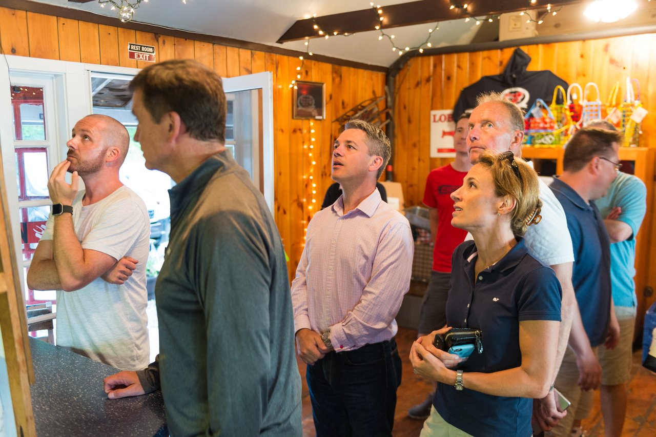 A group of people looks at a menu or board inside a restaurant, deciding on their lobster dinner.