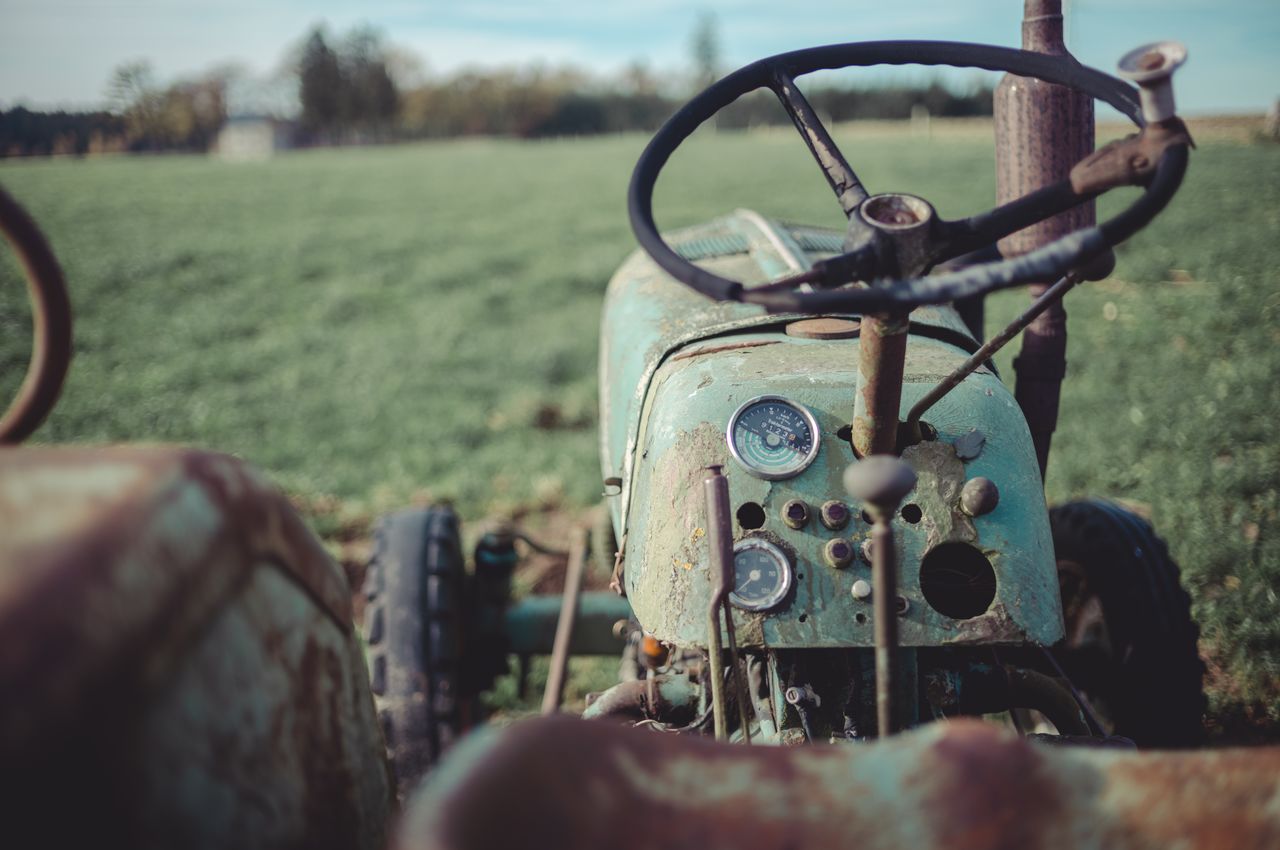 An aged green tractor in a grass field, showing signs of rust.