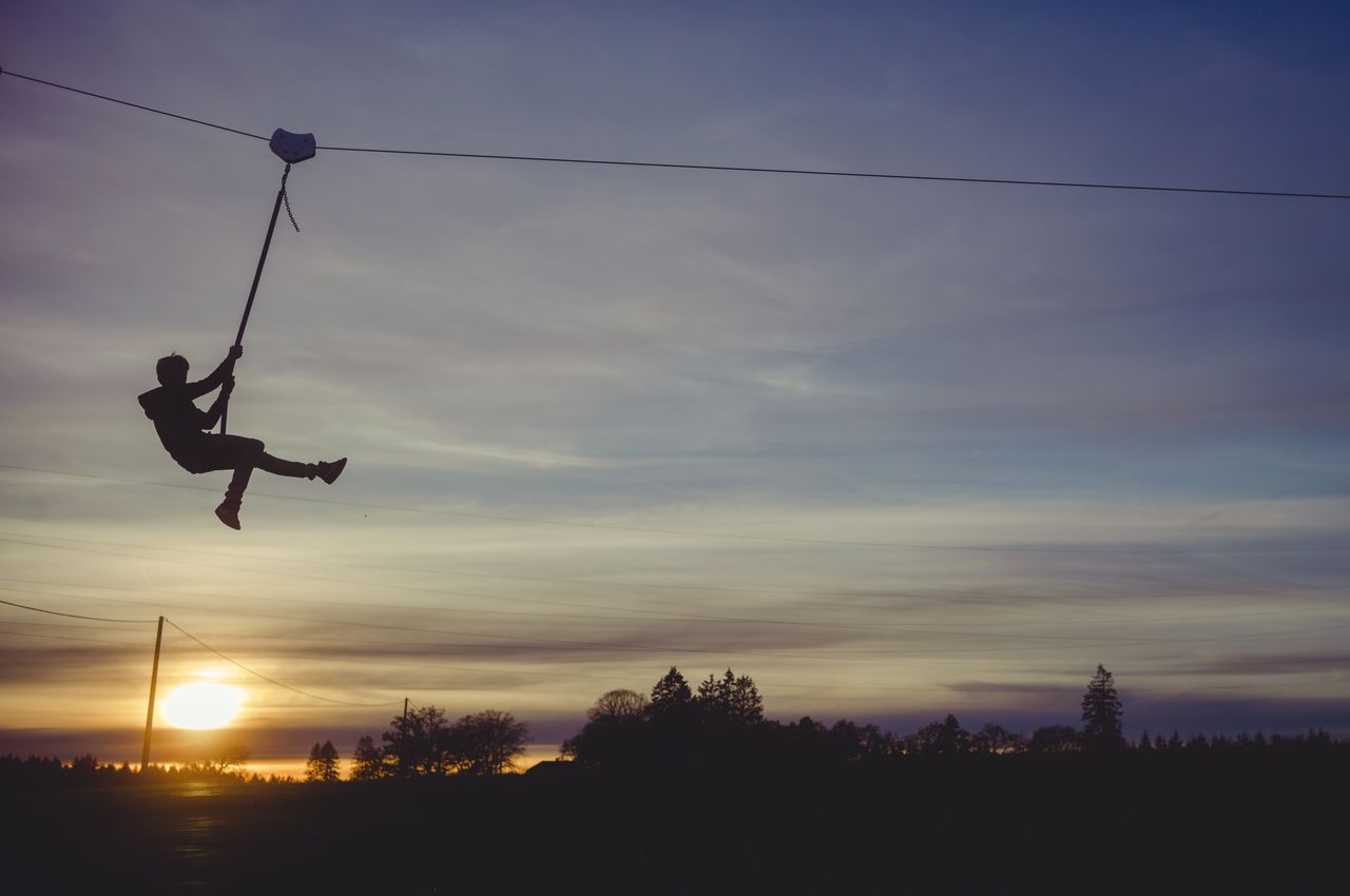 The silhouette of a child ziplining against the sunset.