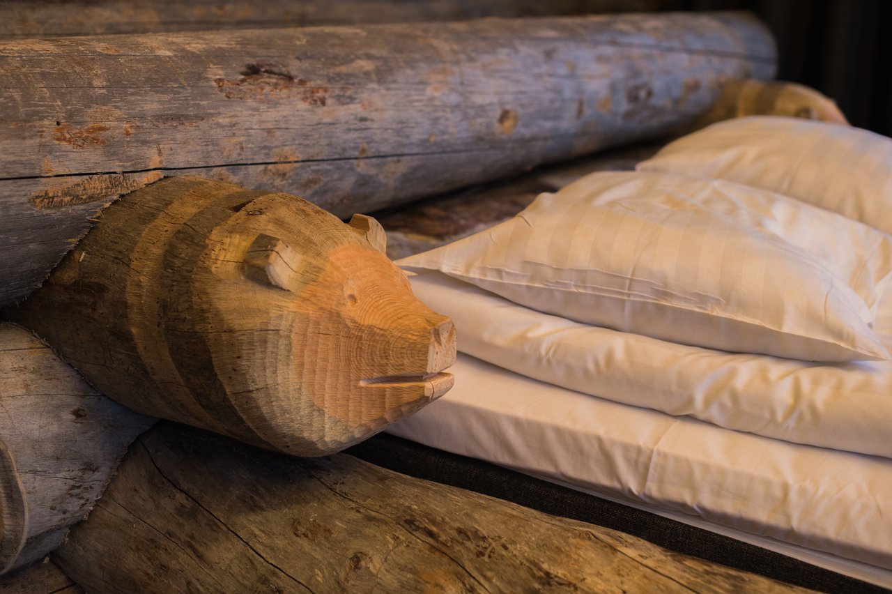 A log cabin bed with white pillows and a carved wooden bear head as part of the bed frame.