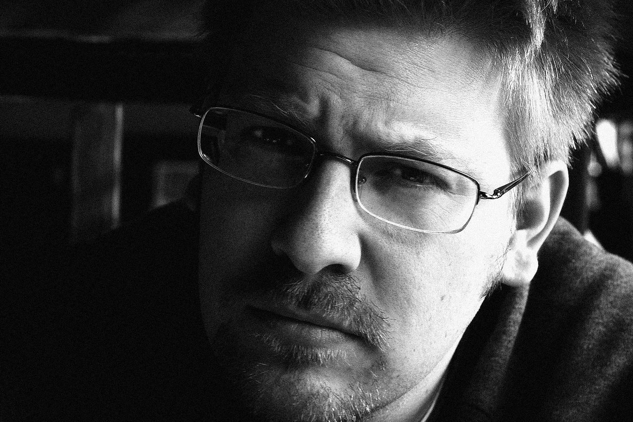 Black and white close-up of a man with glasses, looking seriously at the camera.