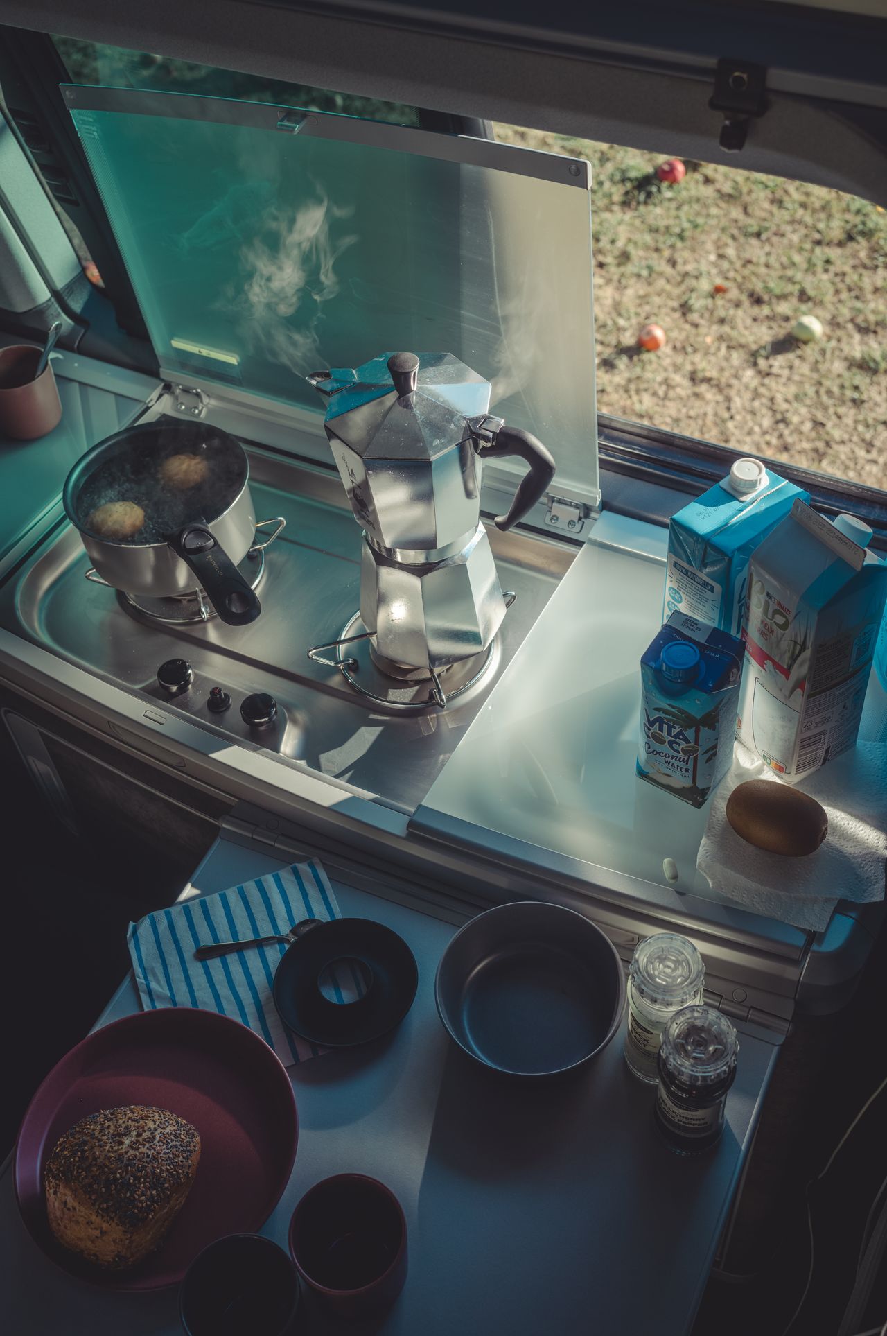 Cooking eggs and brewing coffee in the van’s kitchen, with apples from a nearby tree visible outside the window.