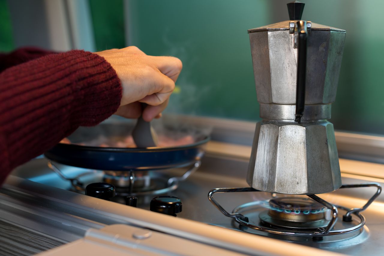 Klaas making breakfast with a moka pot and frying pan in a Volkswagen California camper.