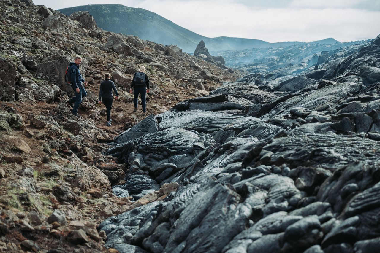 Three hikers walk along a rocky path beside hardened lava at Gerlingadalur volcano in Iceland.