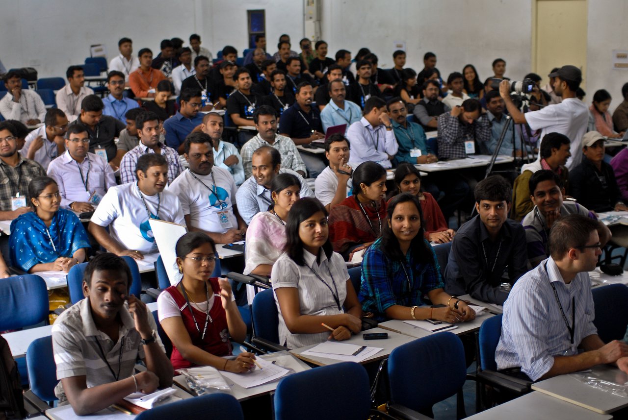 A large group of attendees sits in a conference room, listening and taking notes at Drupalcamp Deccan.